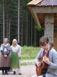 Magnus Larsson spelar gitarr. Mor och dotter Skogholm tittar p&aring;.